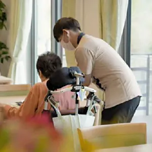 利用者と会話しながら車椅子を押す施設職員の後ろ姿